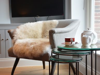 A chair with a fur throw beside nested glass tables with a teapot cup and creamer at Sea Crest in Aldeburgh