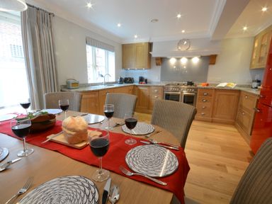 A kitchen with wooden cabinets a dining table set with plates glasses of red wine and bread at Sea Crest in Aldeburgh
