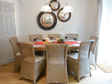 A dining room with a wooden table and wicker chairs set with wine glasses and plates at Sea Crest in Aldeburgh