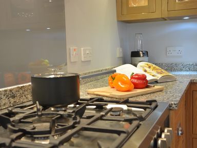 A kitchen countertop with a cutting board holding bell peppers a blender an open cookbook and a pot on a stove at Sea Crest in Aldeburgh