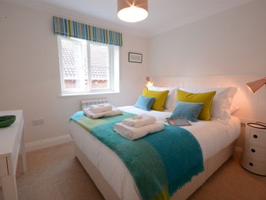 A bedroom with a bed with white sheets green and blue blankets and pillows beside a window at Sea Crest in Aldeburgh