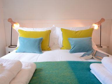 A bed with green and blue cushions white towels and lamps on bedside tables at Sea Crest in Aldeburgh