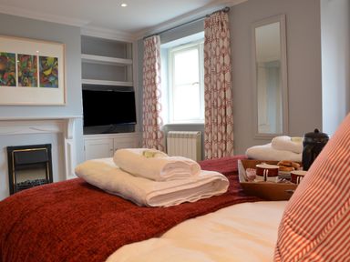 A bedroom with a bed towel trays and cups a fireplace a television and a window with patterned curtains at Sea Crest in Aldeburgh