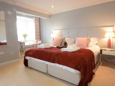A bedroom with a double bed red blanket and pillows bedside lamps and a window with a flower pot at Sea Crest in Aldeburgh