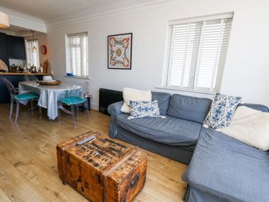 A living room with a gray sofa and wooden chest coffee table next to a dining table with transparent chairs at Flat 7 Sand Acres in Canford Cliffs