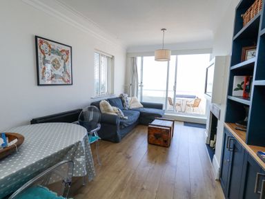 A living room with a blue sofa and wooden chest coffee table next to a dining table with polka dot tablecloth at Flat 7 Sand Acres in Canford Cliffs