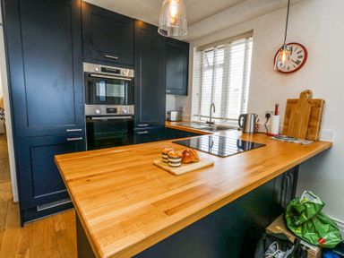 A kitchen with wooden countertops black cabinets built in oven and microwave and a window at Flat 7 Sand Acres in Canford Cliffs