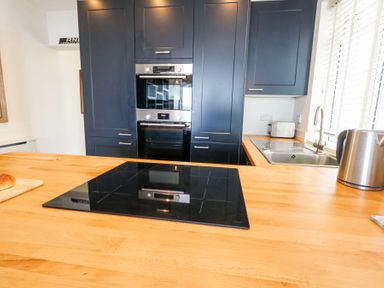 A kitchen with black cabinets, built-in oven, wooden countertop with induction cooktop, stainless steel sink, kettle, and toaster at Flat 7 Sand Acres in Canford Cliffs