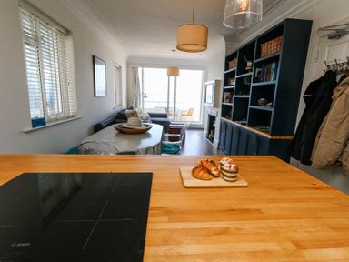 An open living space with a kitchen counter, a dining table with chairs, a sofa, shelves, and a balcony at Flat 7 Sand Acres in Canford Cliffs