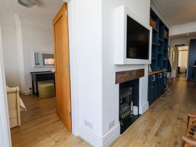 A hallway with wooden floor leading to a room with a desk and ottoman and a television mounted above a fireplace at Flat 7 Sand Acres in Canford Cliffs