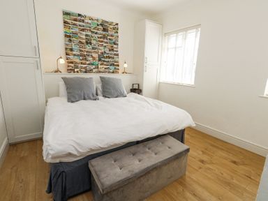 A bedroom with a bed two gray pillows two bedside lamps a photo collage on the wall and a window at Flat 7 Sand Acres in Canford Cliffs