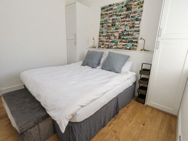 A bedroom with a bed two pillows two bedside lamps a wall collage and storage baskets at Flat 7 Sand Acres in Canford Cliffs