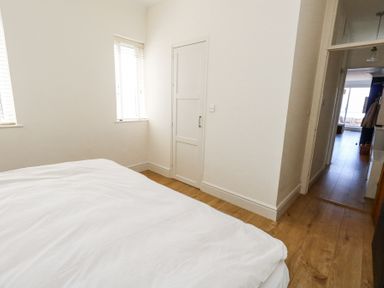 A bedroom with a bed white walls two windows a small door and a hallway leading to another room at Flat 7 Sand Acres in Canford Cliffs