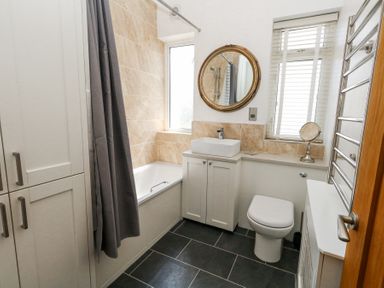 A bathroom with a bathtub shower and curtain a sink with cabinet a round mirror a toilet and a heated towel rail at Flat 7 Sand Acres in Canford Cliffs