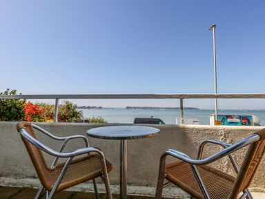 A balcony with two chairs and a round table overlooking the sea at Flat 7 Sand Acres in Canford Cliffs