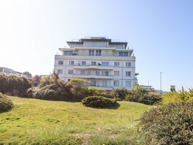A multi-story residential building with balconies surrounded by grass and shrubs at Flat 7 Sand Acres in Canford Cliffs