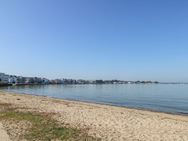 A sandy beach with calm water and buildings along the shoreline at Flat 7 Sand Acres in Canford Cliffs