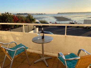 A balcony with two chairs and a small round table overlooking a beach with people and vehicles at Flat 7 Sand Acres in Canford Cliffs