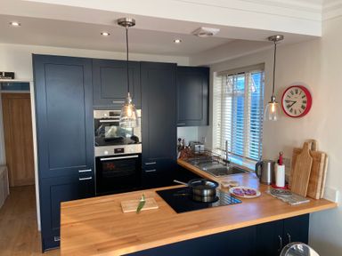 A kitchen with navy cabinets a wooden countertop a stove sink and kitchen utensils at Flat 7 Sand Acres in Canford Cliffs