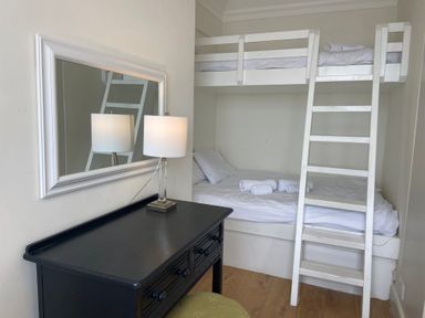 A bedroom with a white bunk bed ladder a black desk with a lamp and a mirror on the wall at Flat 7 Sand Acres in Canford Cliffs