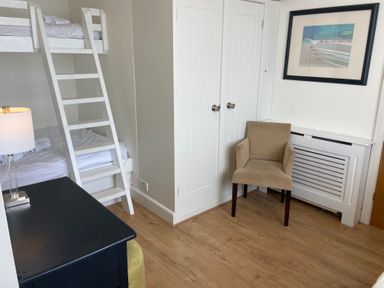 A bedroom with a bunk bed a beige chair a black desk a lamp and a framed picture on the wall at Flat 7 Sand Acres in Canford Cliffs