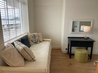 A room with a daybed near a window and a black dressing table with a mirror and lamp at Flat 7 Sand Acres in Canford Cliffs
