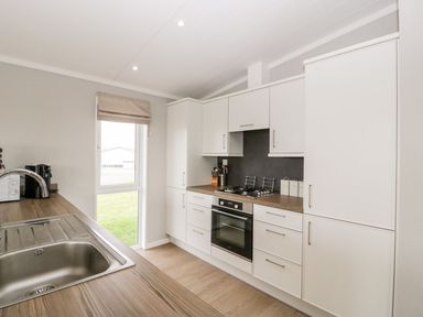 A kitchen with white cabinets a stove an oven a sink a window and wooden countertops at Summerdown in Brean