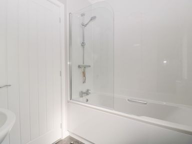 A bathroom with a bathtub and shower and a white door at Summerdown in Brean