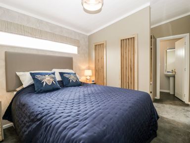 A bedroom with a bed with blue quilt and bee pillows near two wooden wall niches and an open door leading to a bathroom at Summerdown in Brean