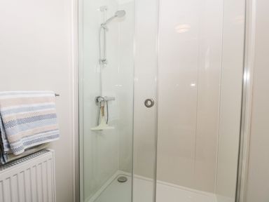 A shower enclosure with a handheld showerhead and glass door next to a towel rack with striped towels at Summerdown in Brean