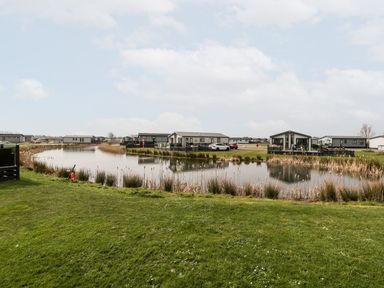 Small houses near a pond with grassy area in the foreground at Summerdown in Brean
