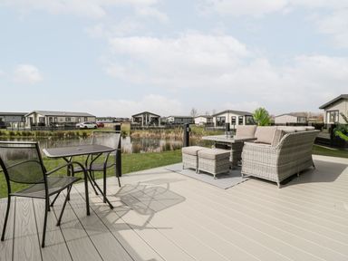 A patio with seating and tables overlooking a pond with houses in the background at Summerdown Brean