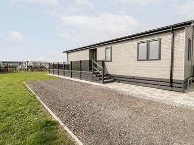 A single-story modular home with a gravel driveway a grass lawn and a black fence at Summerdown Brean
