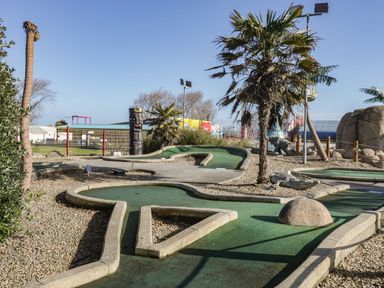 An outdoor mini golf course with palm trees and tiki statues at Summerdown in Brean