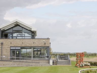 A modern building with glass windows and stone walls with an outdoor seating area and a flower planter on a lawn at Summerdown in Brean