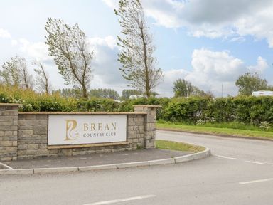 A stone wall with a sign for Brean Country Club with trees and bushes behind it in Brean