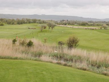 A golf course with green grass water hazard and hills in the background at Summerdown in Brean