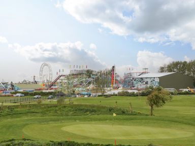 A golf course putting green with amusement park rides and a ferris wheel in the background at Summerdown in Brean
