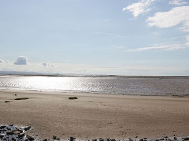 A sandy beach with scattered rocks and patches of grass by the water with clouds in the sky at Summerdown in Brean