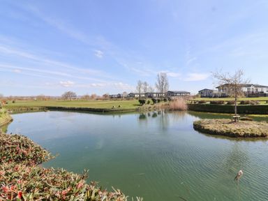 A pond with an island and grass surrounded by houses under a blue sky at Summerdown in Brean