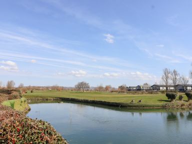 A golf course with a water hazard and two birds on the grass near houses at Summerdown in Brean