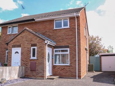 A brick semi detached house with white doors and windows next to a driveway and garage at Sweetacres in Hemsby