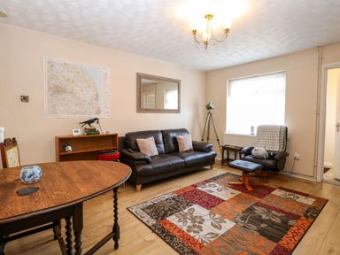 A living room with a brown leather sofa two chairs a wooden table a colorful rug and a tripod lamp at Sweetacres in Hemsby