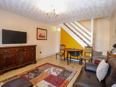 A living room with a television on a wooden cabinet a small round table with two chairs a staircase and a brown leather sofa at Sweetacres in Hemsby