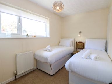 A bedroom with two single beds white bedding a window and a chair at Sweetacres in Hemsby