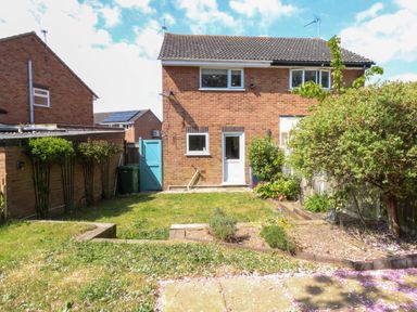 A backyard with grass a garden bed a tree and a brick house with white doors and windows at Sweetacres in Hemsby