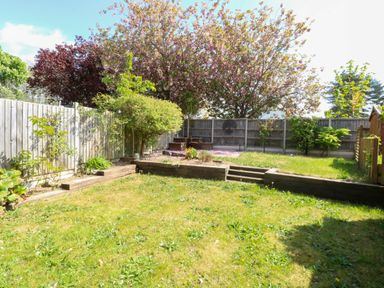 A garden with grass trees wooden steps and a wooden fence at Sweetacres in Hemsby
