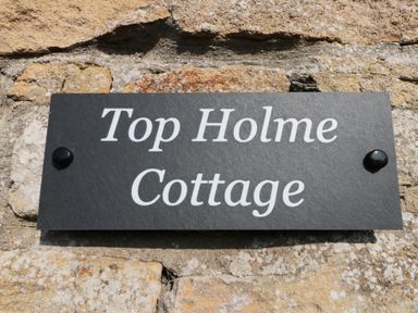 A black sign with white text reading Top Holme Cottage mounted on a stone wall at Top Holme Cottage in Newbald