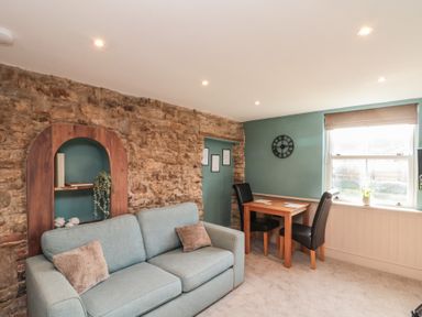 A sitting room with a blue sofa and wooden table with two chairs near a window at Top Holme Cottage in Newbald