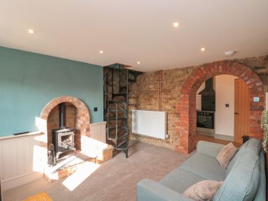 A living room with a wood stove in a brick archway and a spiral staircase at Top Holme Cottage in Newbald